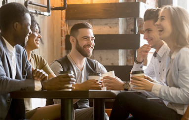 A group of young adults sitting at a table smiling and talking over coffee